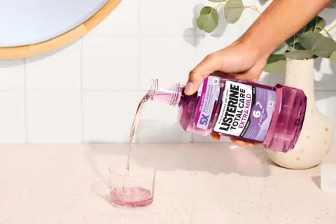 Ręka wylewa fioletowy płyn Listerine Total Care Extra Mild do szklanki. Poznaj listerine skład i ciesz się świeżym oddechem.