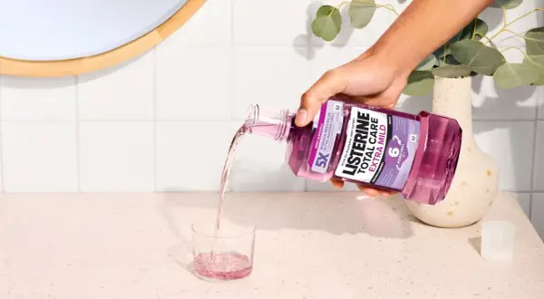 Ręka wylewa fioletowy płyn Listerine Total Care Extra Mild do szklanki. Poznaj listerine skład i ciesz się świeżym oddechem.