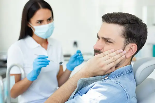 Mężczyzna z bólem policzka u dentysty, który bada jego dziąsła. Może to być objaw pogłębiających się kieszonki dziąsłowe.