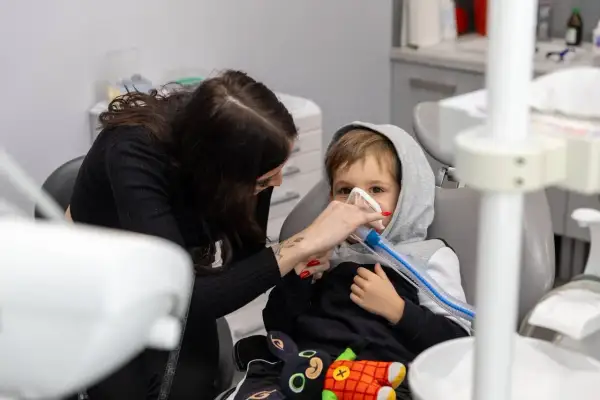 Chłopiec w masce znieczulającej, kobieta pomaga mu, łagodząc ból dziąsła po znieczuleniu.