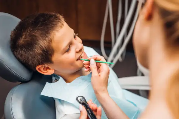 Chłopiec uśmiecha się, gdy dentystka bada jego zęby. Nie martwi się wypadaniem zębów, bo wie, że to naturalny proces.