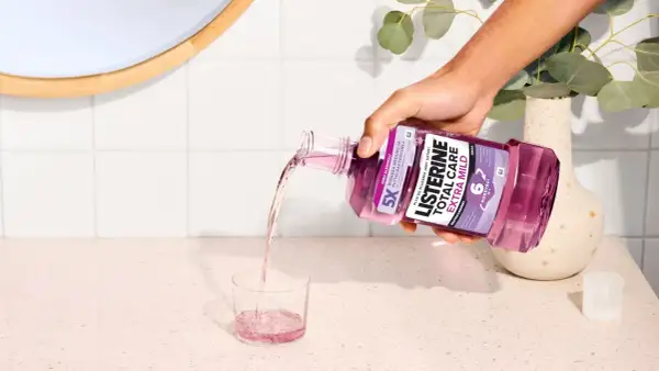 Ręka wylewa fioletowy płyn Listerine Total Care Extra Mild do szklanki. Poznaj listerine skład i ciesz się świeżym oddechem.